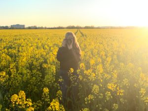Young girl stands in the evening sun with a camera in the rape field Young girl stands in the evening sun with a camera in the rape field